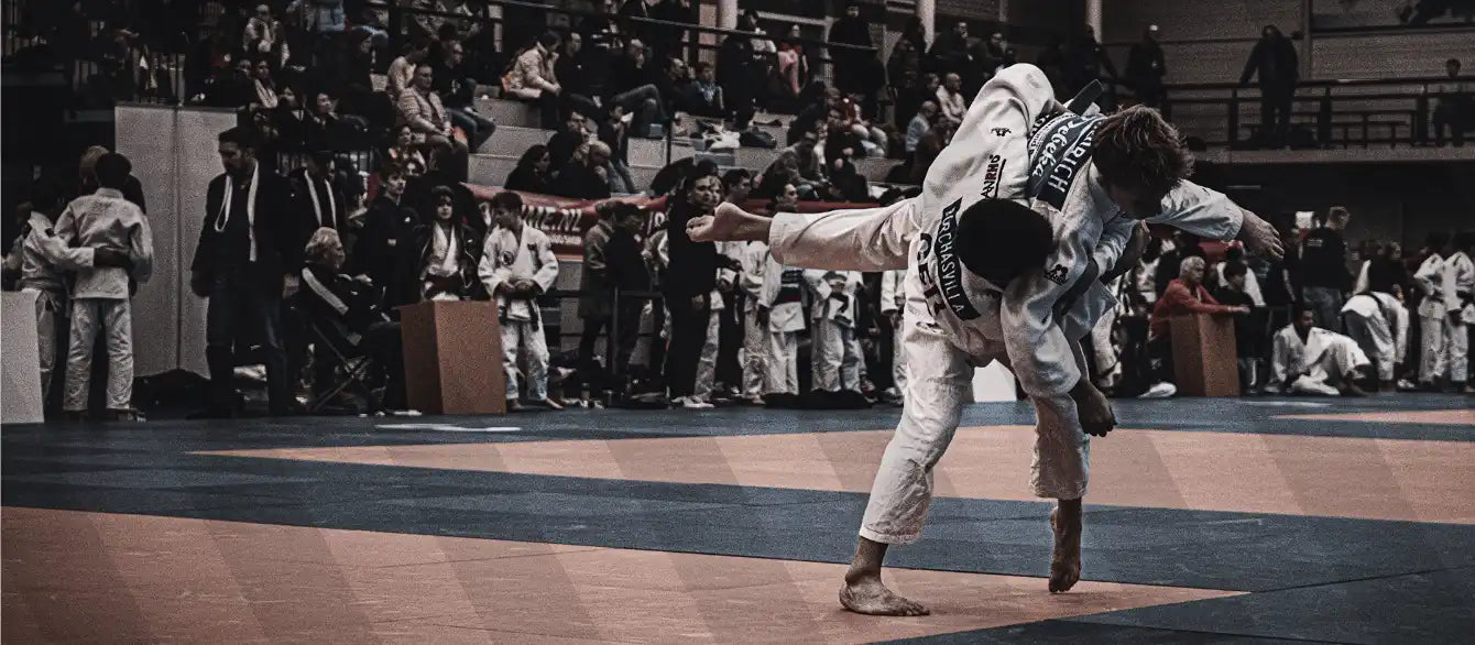 Judokas en kimono blanc effectuant une projection devant un public lors d'un match